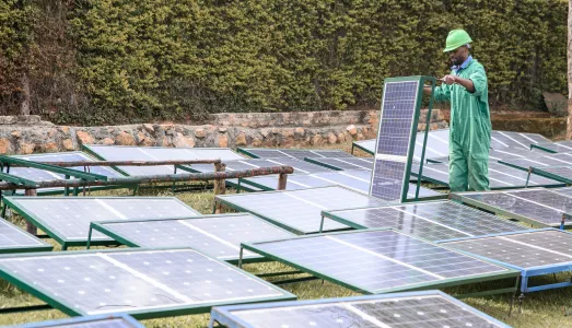 A technician in a green jumpsuit and hard hat inspects solar panels in Uganda during the closeout of the SEFFA project.