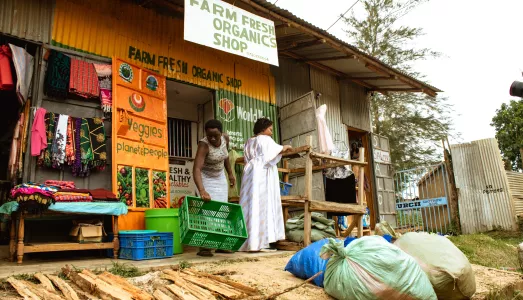An external view of the Farm Fresh Organics shop, where Mildren Oketch, aided by an employee, receives sacks of vegetables from farmers for sale in Kenya.